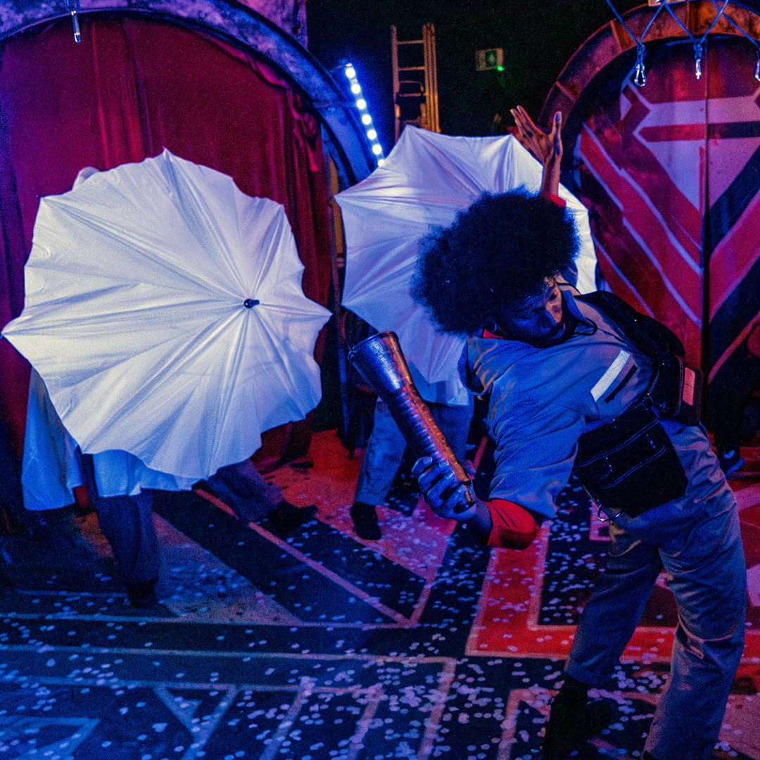 A person acting in a show with two white umbrellas and a confetti cannon.