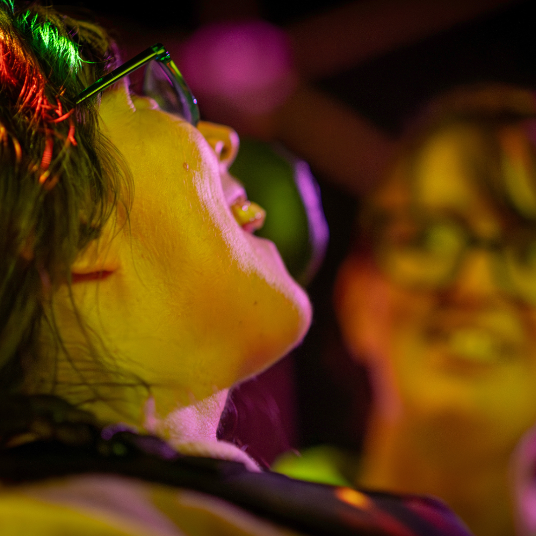 A person smiling with another person blurred in the background smiling too