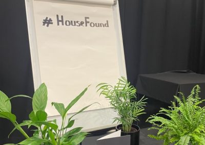 A white billboard surrounded by potted plants with the text "house found"