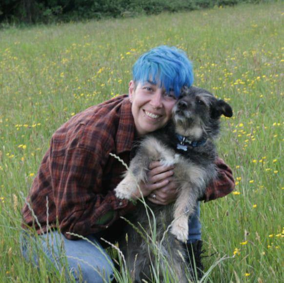 Michaela Garner crouches down cuddling a dog in a field.