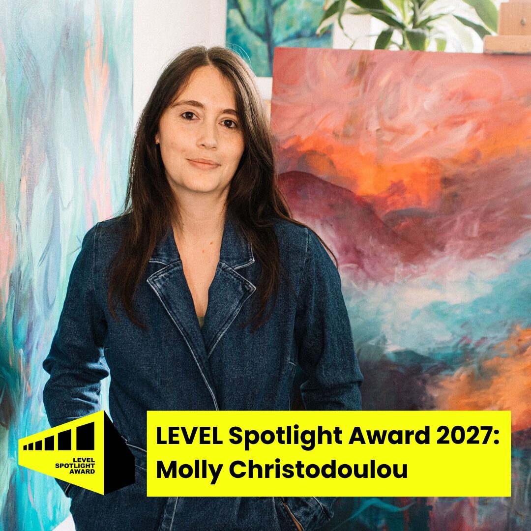 molly c colour spot (1) Molly Christodoulou stands with hands in pockets in an art studio, surrounded by colourful abstract paintings. They have long dark brown hair and wear a dark denim jumpsuit. A bright yellow and black abstract graphic of a corridor sits in the bottom left of the image. Black text on a bright yellow banner reads: LEVEL Spotlight Award 2027 Molly Christodoulou.
